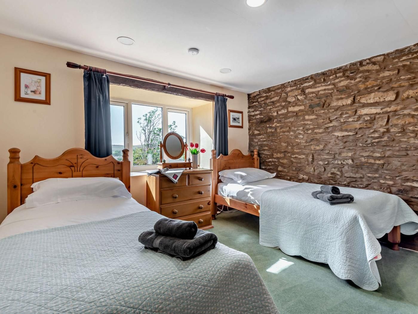 Une chambre avec deux lits, une commode, un miroir et un mur en pierre.