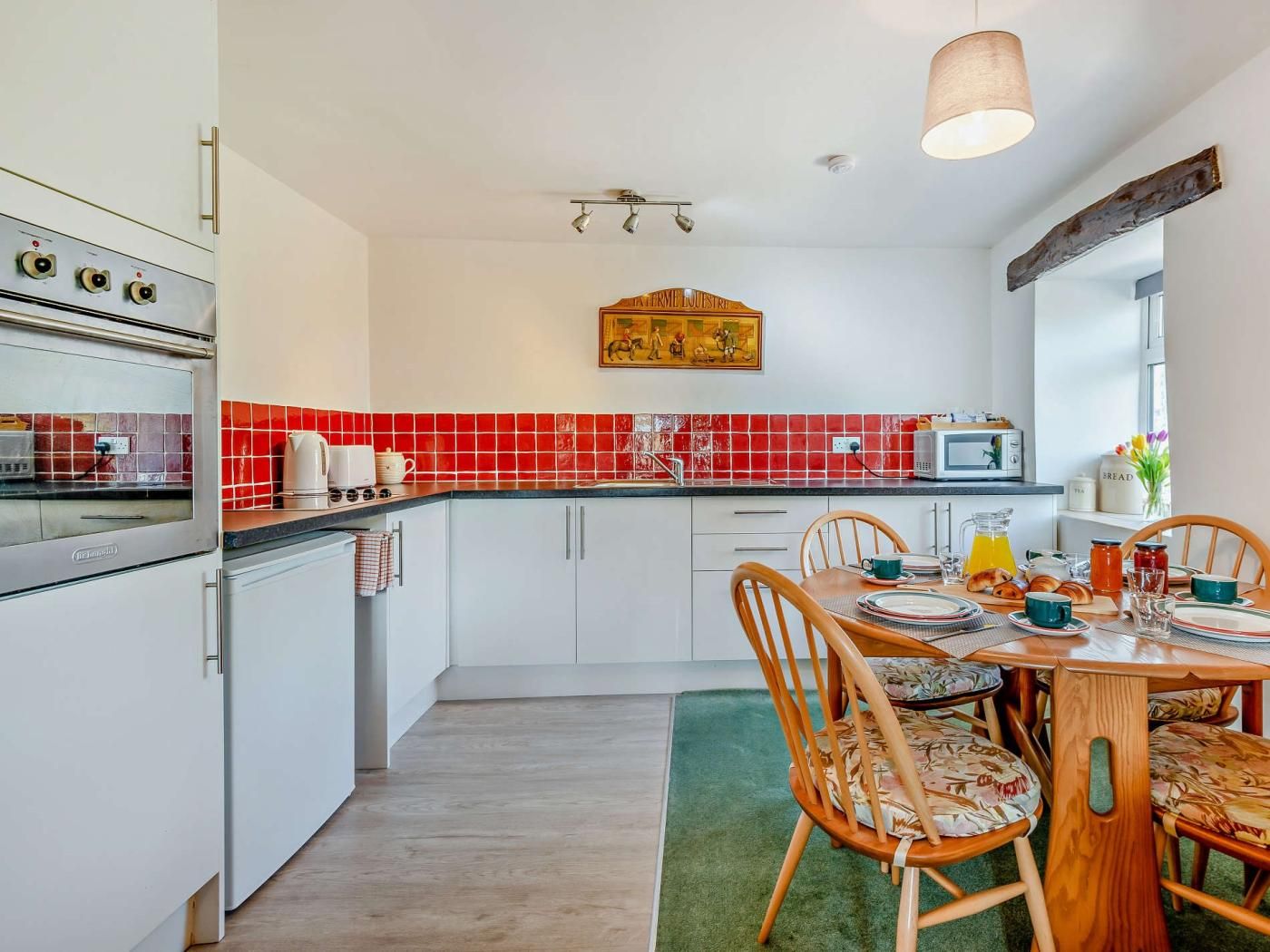 A kitchen with white cabinets, a red-tiled backsplash, a dining table with chairs, and a hanging light fixture.