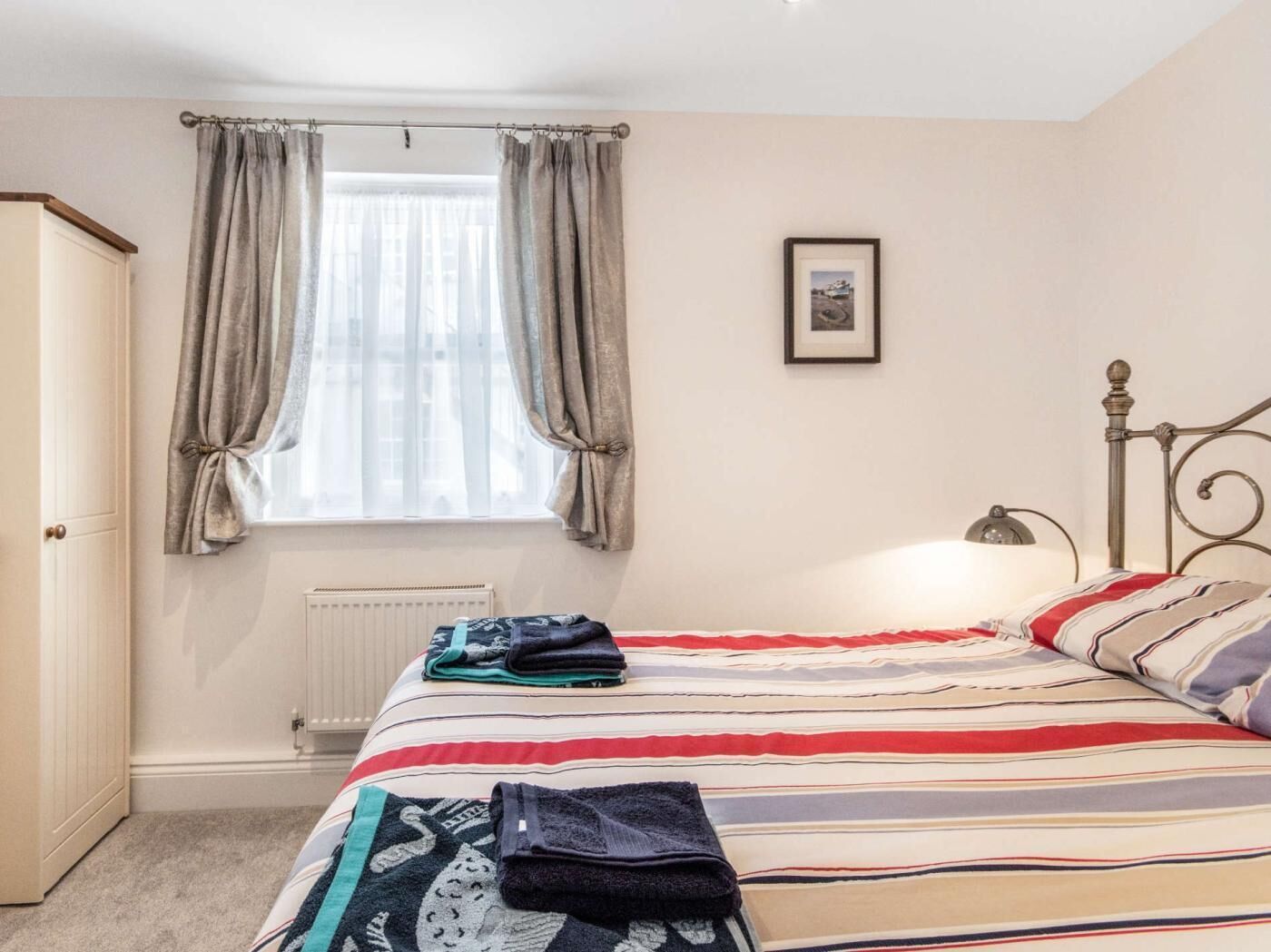 A bedroom with a bed, curtains, a radiator, a framed picture, and a wardrobe.