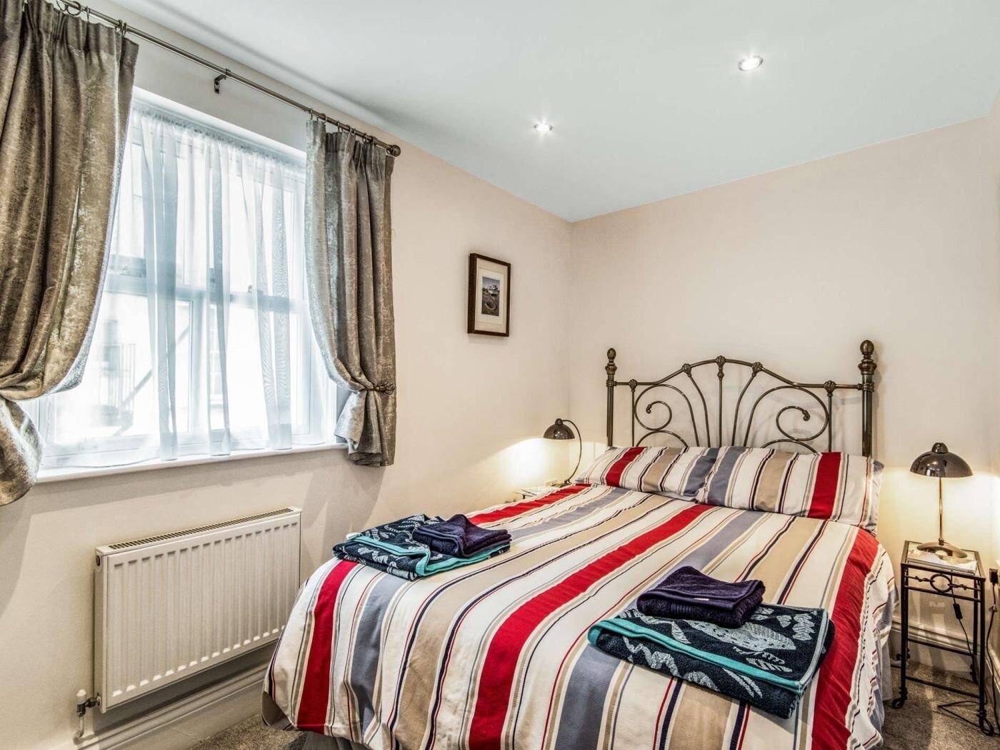 A bedroom with a bed, two bedside lamps, a radiator, and curtains.