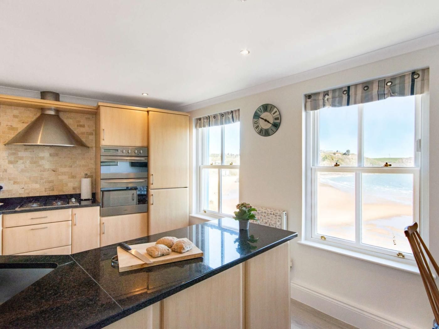 A kitchen with a central island, built-in oven, and a view of the beach through large windows.