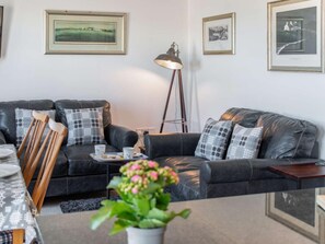 A modern living room with a dark leather sofa, a wooden chair, a small table with a tray of food, and a potted plant. - 2 Bed in Tenby (oc-fb115) (Tenby)