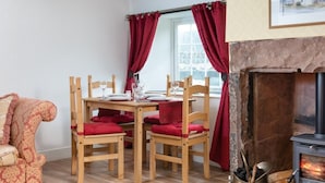 Ein gemütliches Zimmer mit Esstisch, Stühlen, Kamin und einem fensterbepflanzten Fenster.