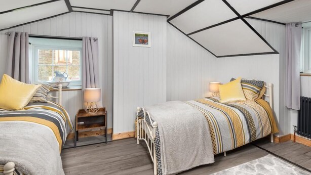 Ein Schlafzimmer mit zwei Betten, einem Fenster mit Vorhängen, einem Heizkörper und einer Decke mit freiliegenden Balken.