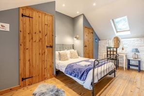 A bedroom with a bed, wooden wardrobe, a small desk, and a stone wall. - 2 Bed in Beaworthy (oc-wvttb) (Ashwater)