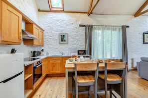 A cozy kitchen with wooden cabinets, a dining table, and a window with curtains. - 2 Bed in Beaworthy (oc-wvttb) (Ashwater)