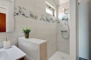 Ein modernes Badezimmer mit Dusche, Waschbecken und einer Topfpflanze.