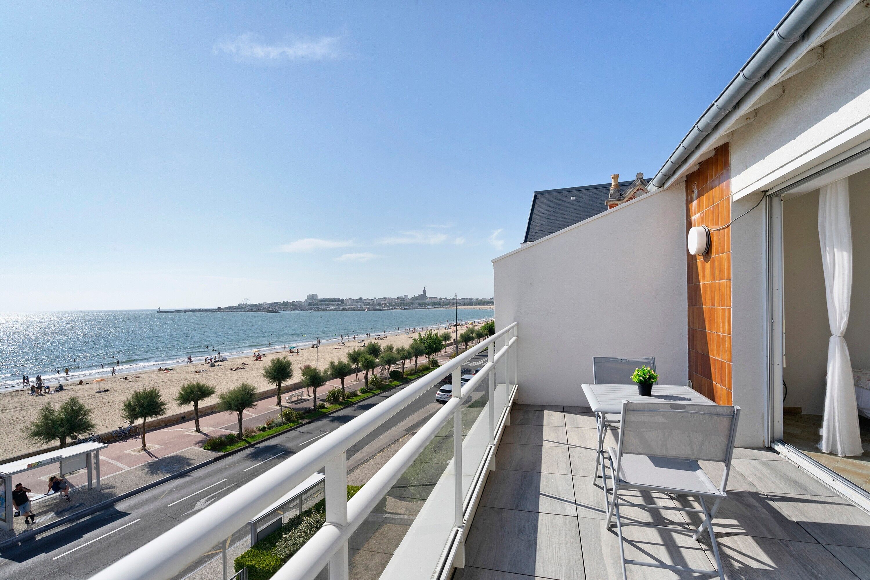 Un balcon donnant sur une plage et la mer, une table avec une chaise et une plante en pot.