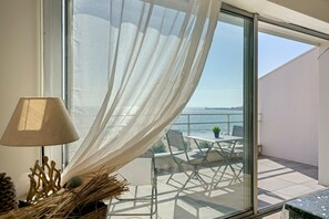 Ein Balkon mit Tisch, Stühlen, einer Lampe und Blick aufs Meer.