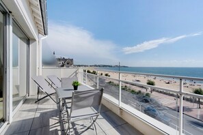 Ein Balkon mit Tisch und Stühlen mit Blick auf einen Strand und das Meer.