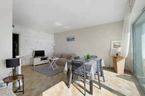 Ein modernes Wohnzimmer mit einer Couch, Fernseher, Esstisch und Dekorationselementen.