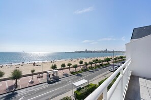 Blick auf die Küste mit Strand, Promenade und einer Straße mit parkenden Autos.