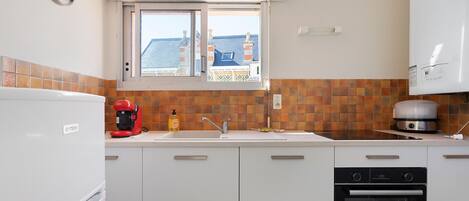Una cocina con armarios blancos, una cafetera Bosch, un fregadero y un horno Beko.