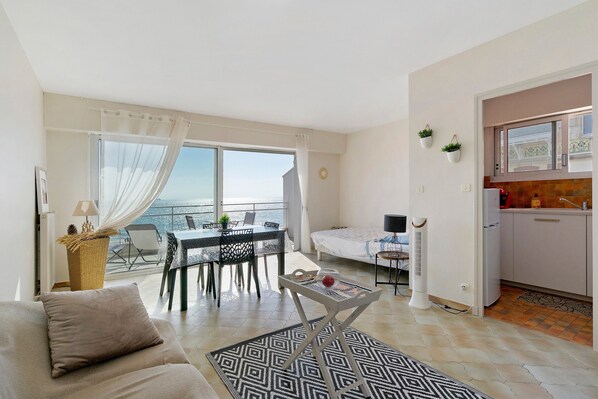 Sala de estar moderna com sofá, mesa de jantar e cadeiras, varanda com vista e pequeno espaço de cozinha.
