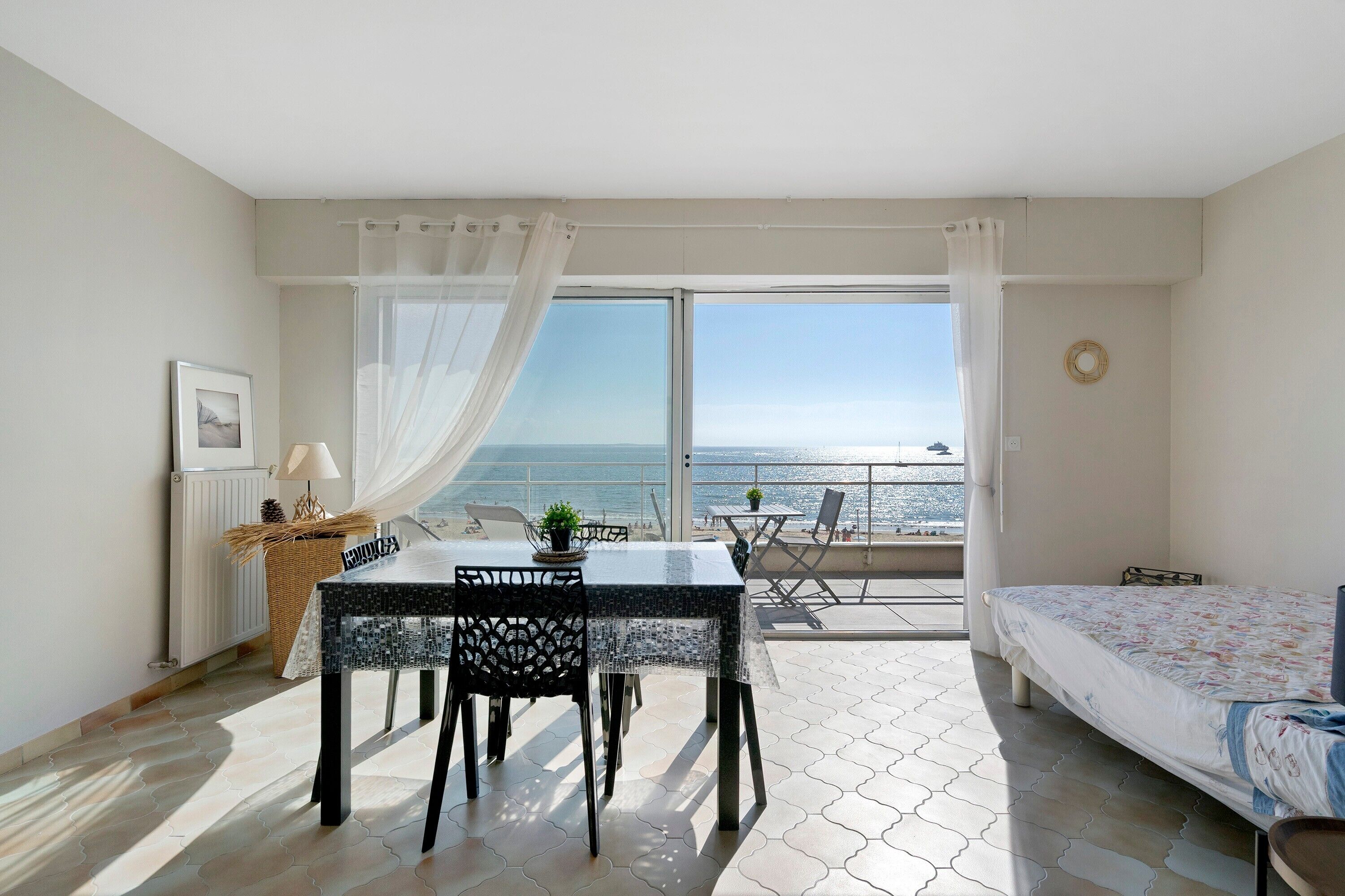 Ein Zimmer mit Esstisch, Stühlen, einem Bett und Meerblick durch große Fenster.