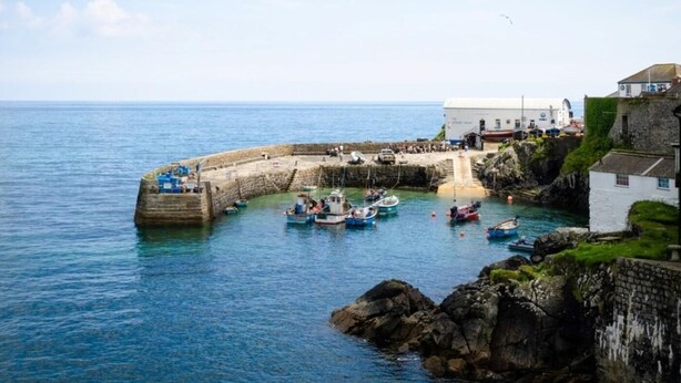 Una cittadina costiera con un molo in pietra, barche e un edificio bianco con tetto verde.