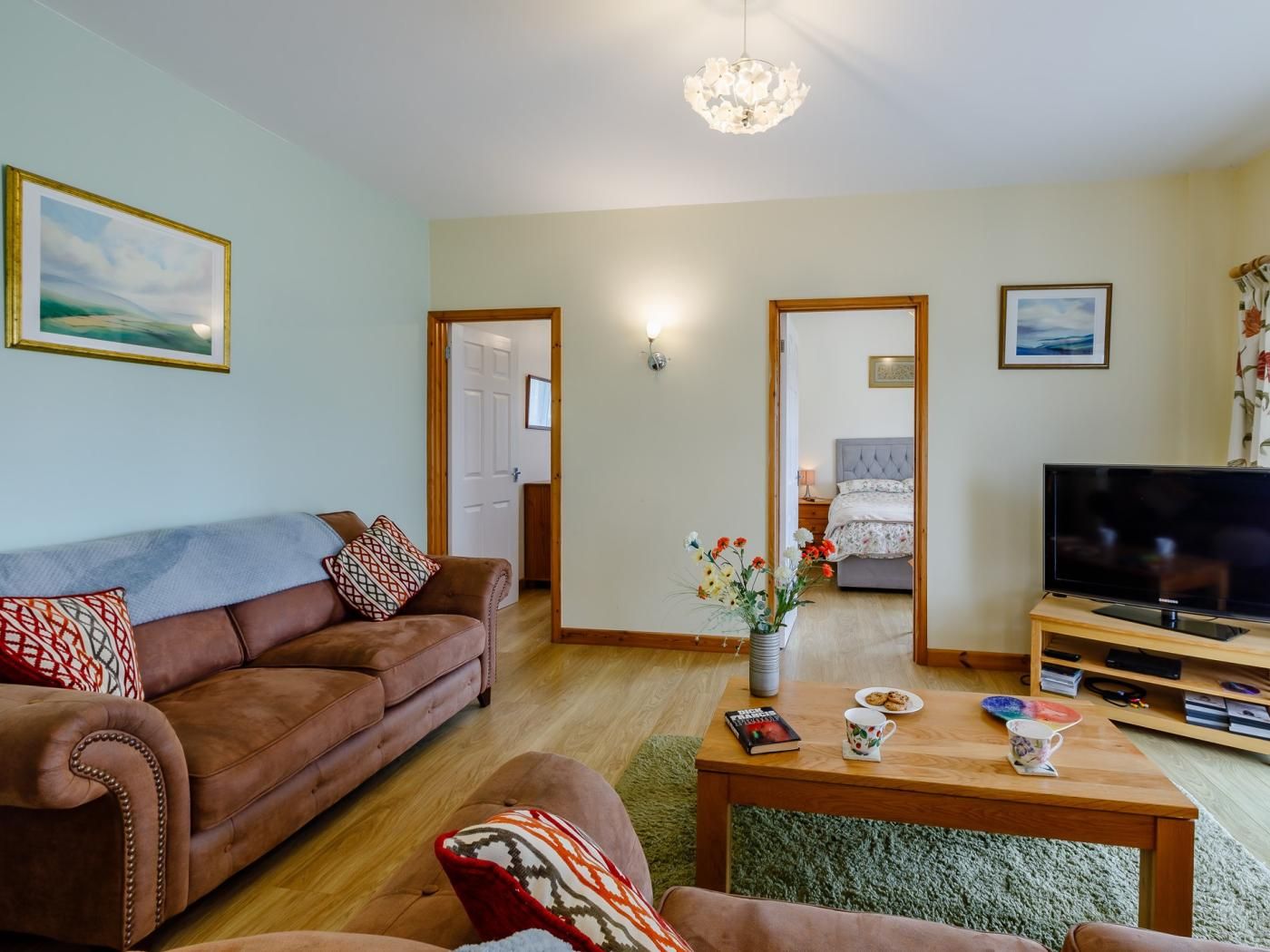 Ein Wohnzimmer mit braunem Sofa, einem Couchtisch, einem Fernseher und einem Bett im Hintergrund.