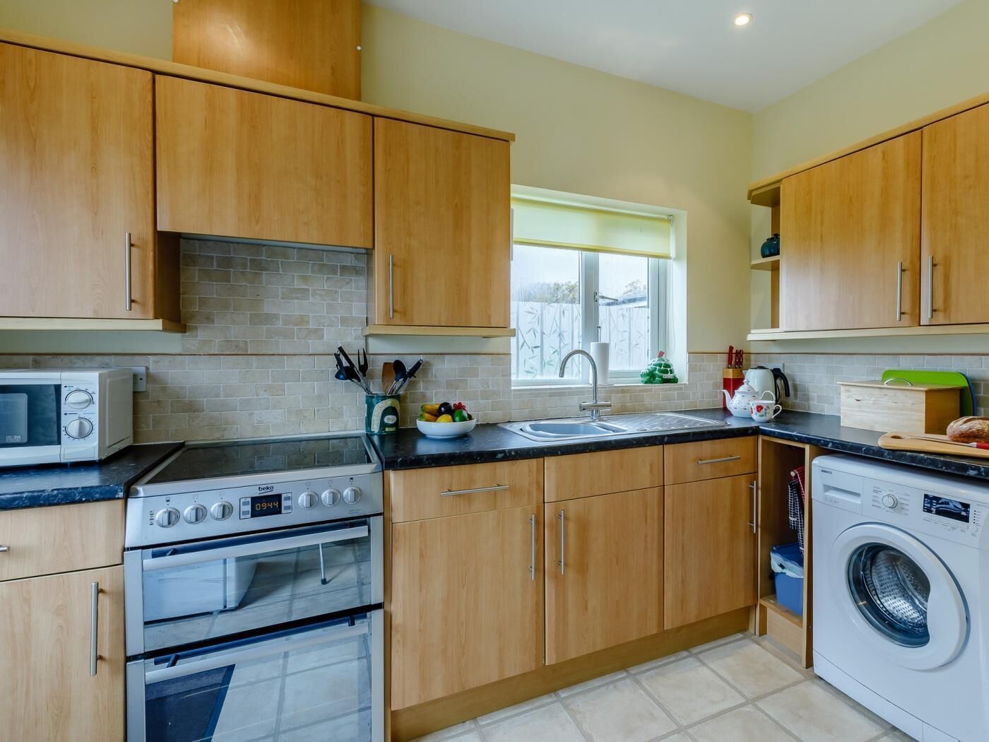 A kitchen with wooden cabinets, a microwave, an oven, a sink, and a washing machine.