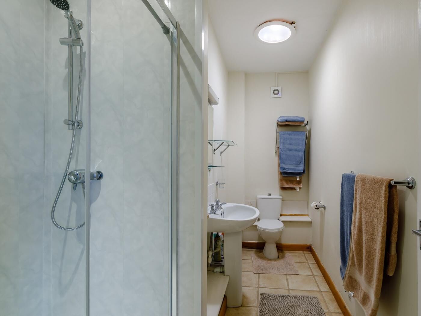 A bathroom with a glass shower enclosure, a sink, a toilet, and a towel rack.