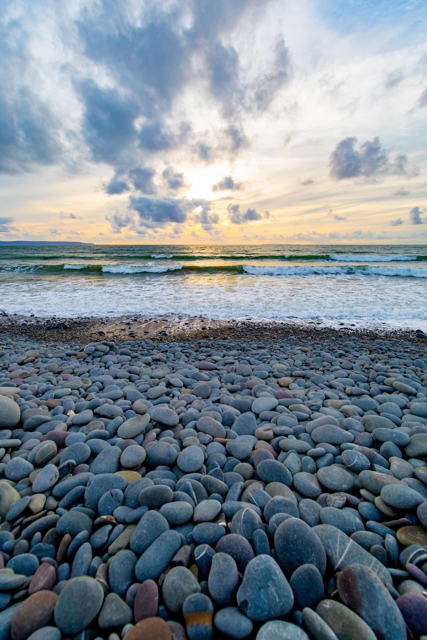 Una playa de guijarros con olas y cielo nublado.
