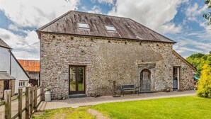 A stone building with a sloped roof, a wooden door, and a bench outside. - 3 Bed in Winkleigh (oc-1450b) (Iddesleigh)
