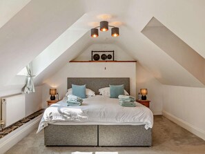 A bedroom with a sloped ceiling, a bed with pillows, a bedside table with a lamp, and a radiator. - 1 Bed in Torrington (oc-annas) (Langtree)