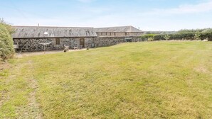 A stone building with a flat roof, a grassy yard, and a clear sky. - 1 Bed in Helston (oc-bbird) (Saint Martin)