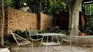 A metal table and chairs set on a paved area with a brick wall and greenery in the background. - The Valley Escape - Unit 2 (Gqeberha)