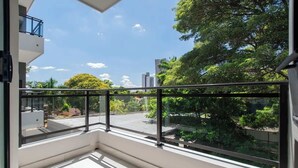 Ein Balkon mit Glasgeländer, Blick auf eine Wohngegend und einen klaren Himmel.