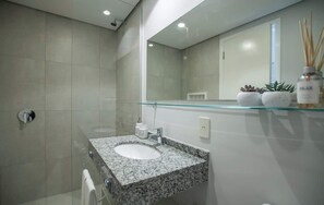 Un baño moderno con lavamanos de granito, estante de vidrio con artículos de aseo y un espejo grande.