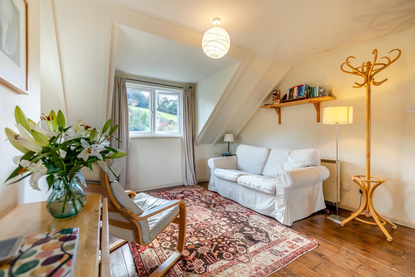 A cozy room with a white sofa, a patterned rug, a wooden chair, a floor lamp, and a bookshelf.