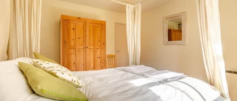 A bedroom with a bed, curtains, a wooden wardrobe, and a mirror.