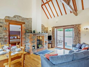 Ein gemütliches Wohnzimmer mit Kamin aus Stein, einem Essbereich mit Holztisch und -stühlen, einem blauen Sofa und einer großen Glasschiebetür, die zu einer Terrassenauslauf führt.