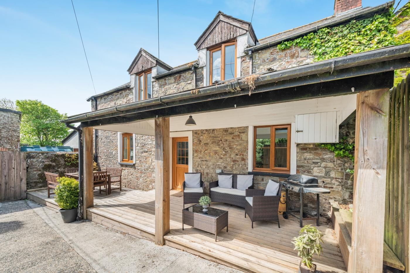 A covered outdoor seating area with a stone wall, wooden deck, and a grill.