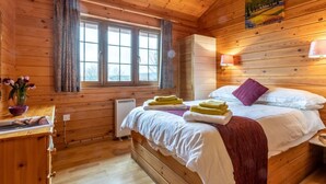 Ein Zimmer in einer Holzhütte mit einem Bett, einem Fenster, einem Heizgerät und einem Bild an der Wand.