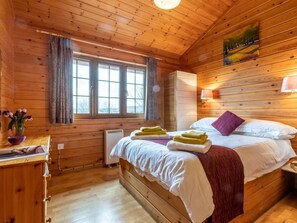A wooden cabin room with a bed, a window, a heater, and a painting on the wall. - 2 Bed in Bideford (oc-00358) (Higher Clovelly)