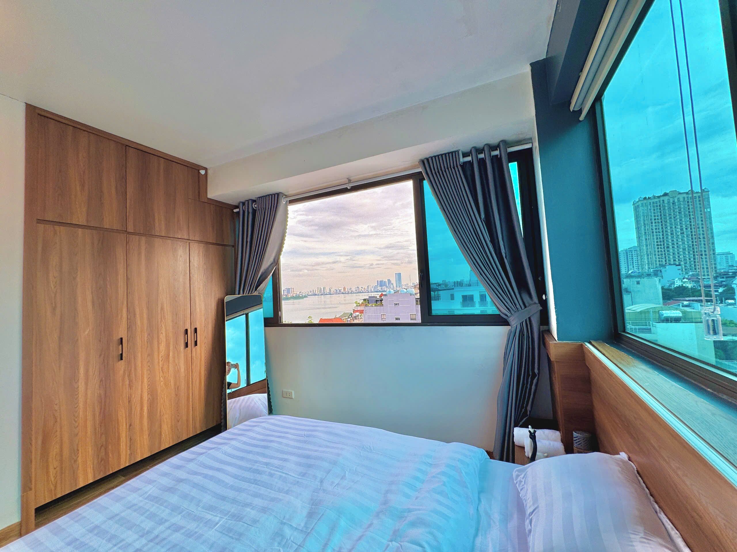 Une chambre d’hôtel avec un lit, une armoire en bois, une fenêtre avec des rideaux et une vue sur la ville.