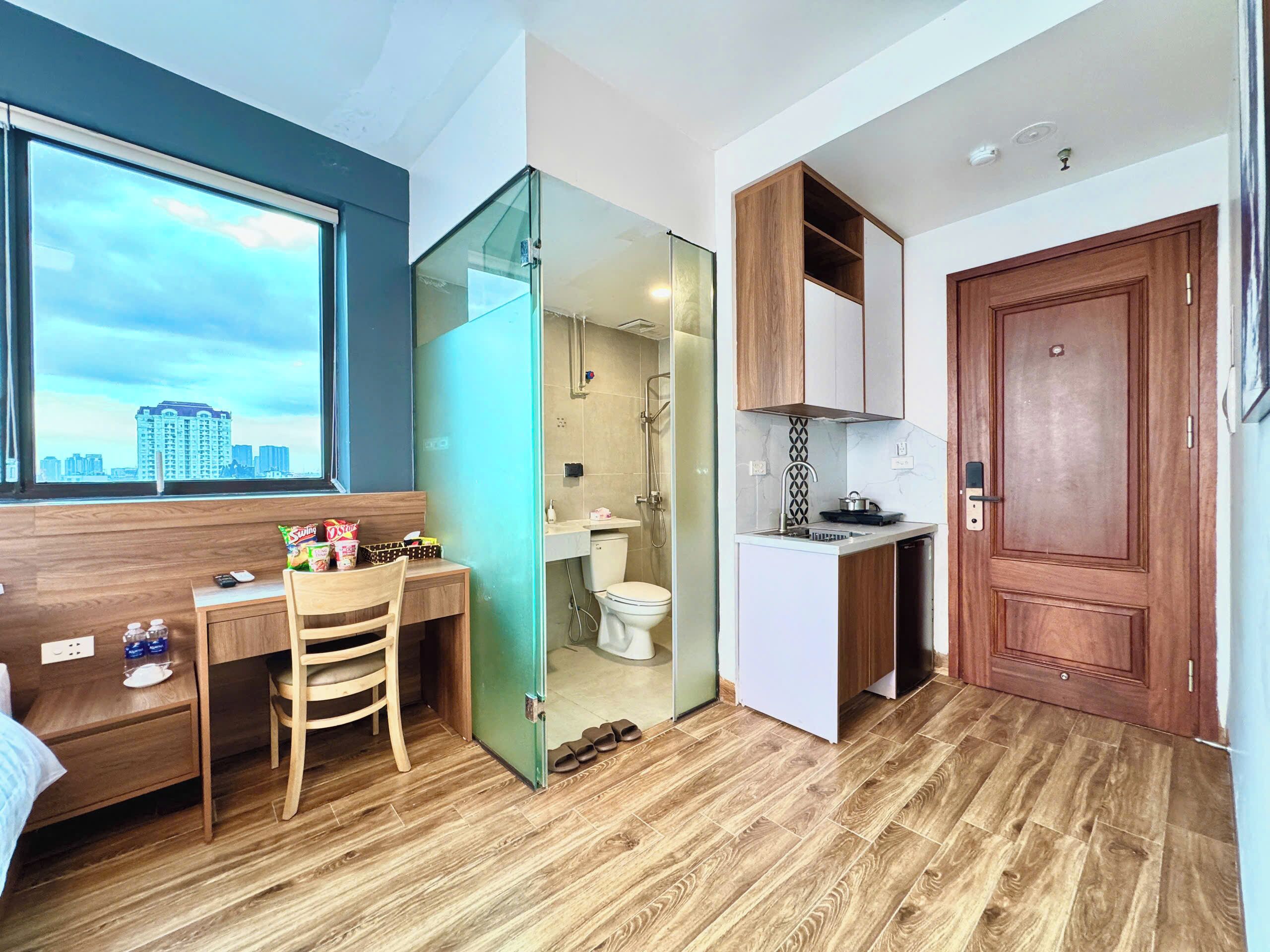 A compact hotel room with a desk, chair, and a view of the city through a window.
