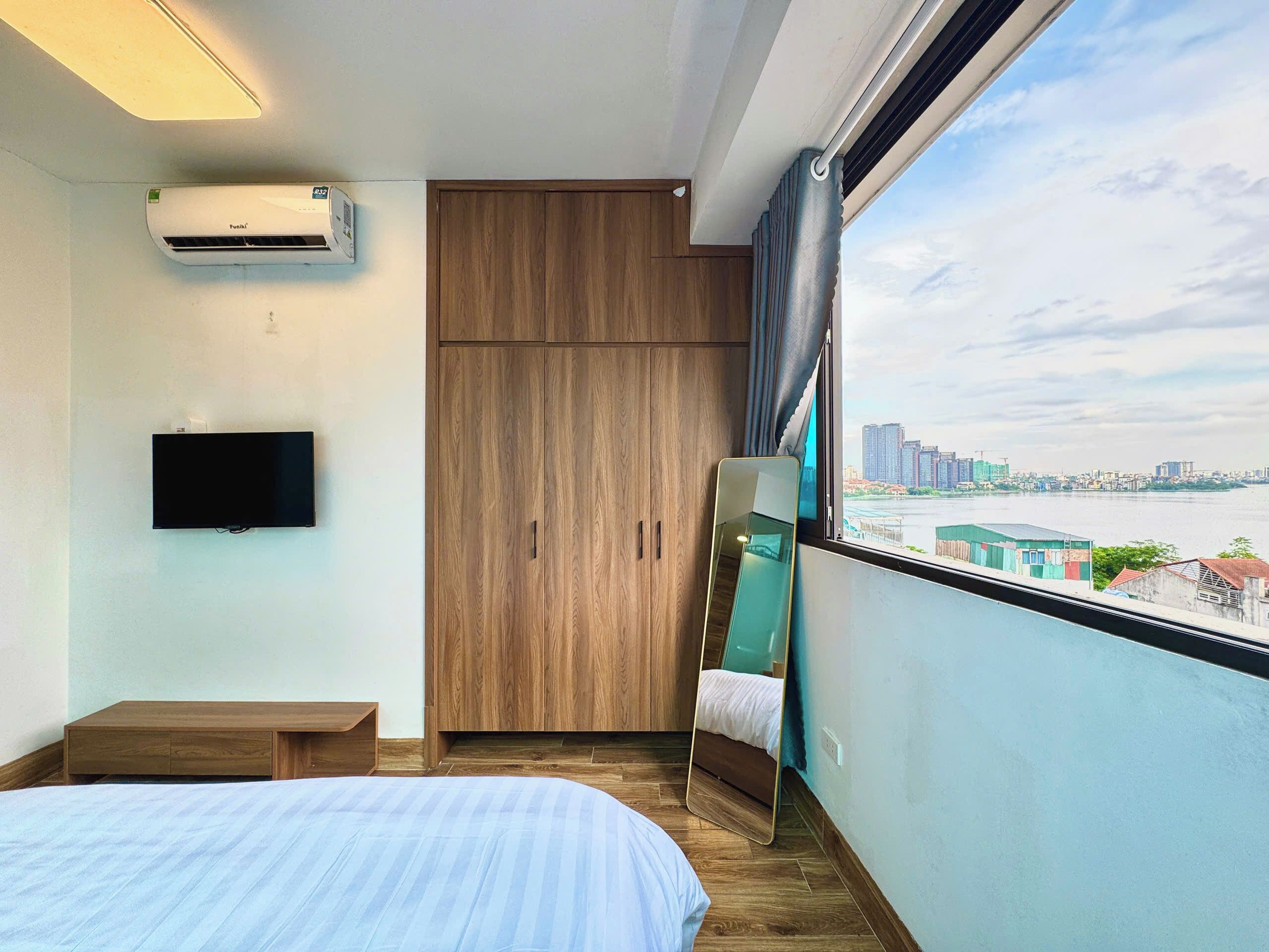 Une chambre avec un lit, une télévision, un climatiseur, une armoire, un miroir et une vue sur la ville.