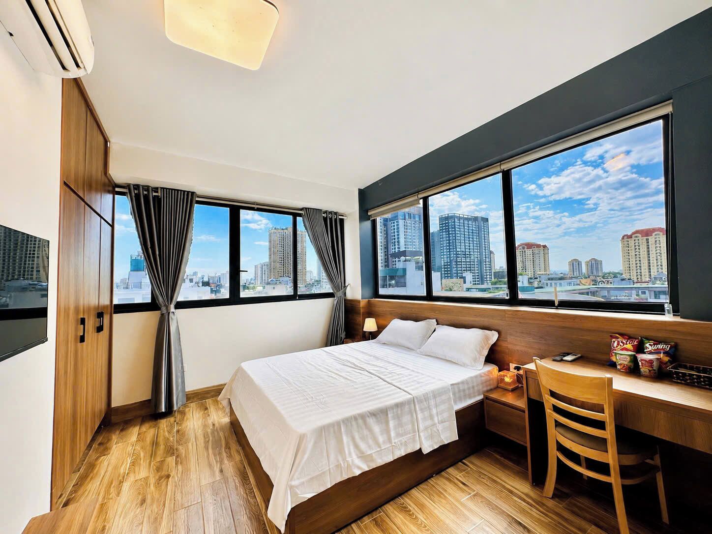 Een hotelkamer met een bed, bureau, stoel, televisie en grote ramen met uitzicht op de stad.