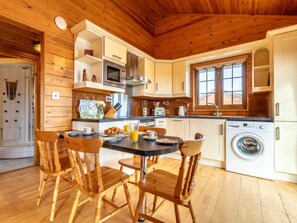 A wooden interior with a dining table, chairs, a microwave, a washing machine, and a window. - 2 Bed in Bideford (oc-00362) (Higher Clovelly)