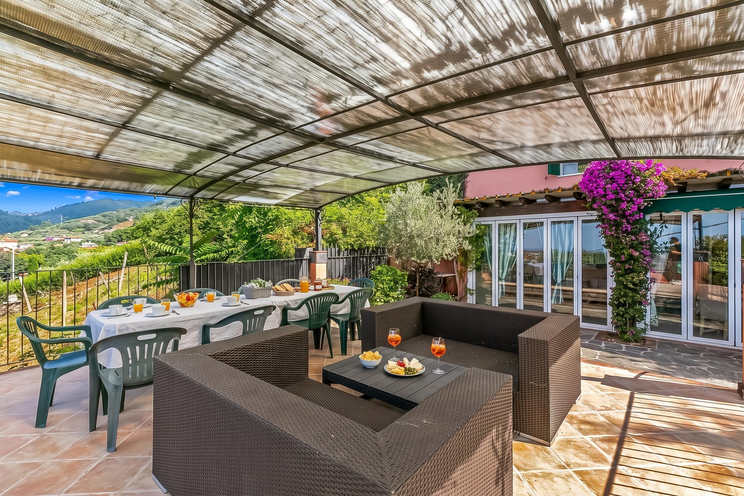 Una terrazza esterna con zona salotto coperta, tavoli da pranzo e vista sulla campagna.