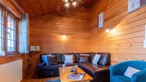 Et hyggeligt interiør i en træhytte med trægulv, en sofasæt, en blå lænestol og et bord med et magasin.