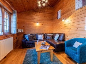Ein gemütliches Blockhaus-Interieur mit Holzboden, einer Sofagarnitur, einem blauen Sessel und einem Tisch mit einer Zeitschrift.