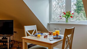 Een eethoek met een tafel, stoelen, een televisie en een raam met tulpen.