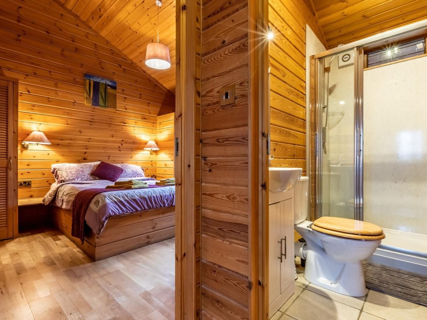 A wooden cabin interior with a bed, a bathroom with a toilet and shower, and wooden walls.
