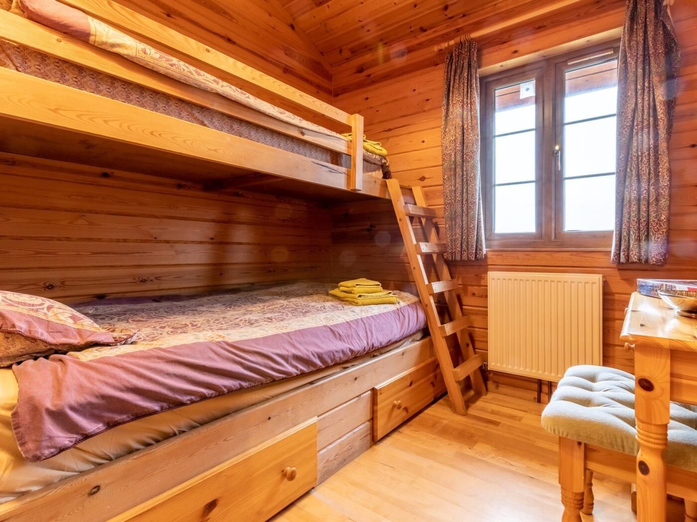 Une chambre dans un chalet en bois, avec des lits superposés, un bureau, une chaise et une fenêtre avec des rideaux.