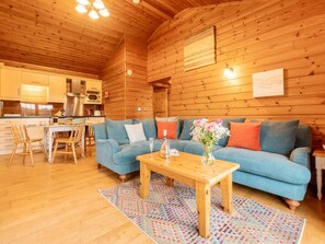 Ein gemütliches Blockhaus-Interieur mit Holzbalkendecke, einem blauen Sofa, einem Holztisch und einer Küchenzeile.