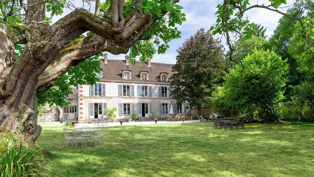 Ein großes, zweistöckiges Haus mit weitläufigem Rasen, Gartenmöbeln und einer Hängematte.