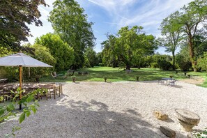 Un patio de grava con mobiliario exterior, rodeado de árboles y vegetación.